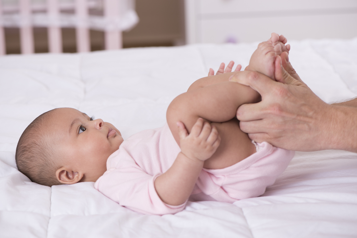 baby on her back looking at a parent with their hands on the baby's legs