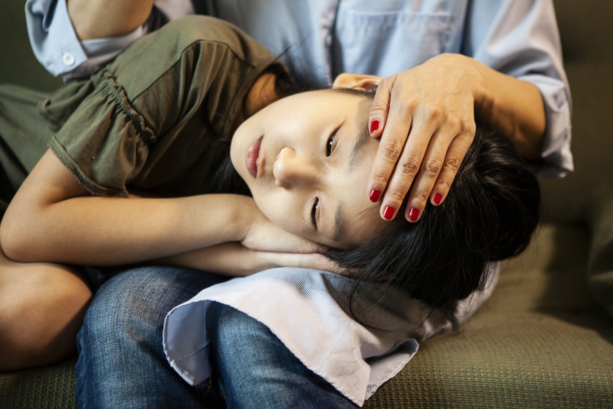 Young girl laying head in a parent's lap, feeling sick