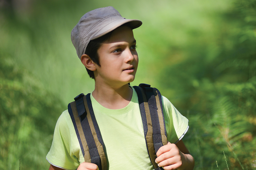 boy wearing a hat and backpack surrounded by green vegetation