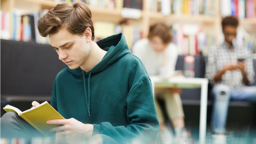 Student guy reading a book in a library 