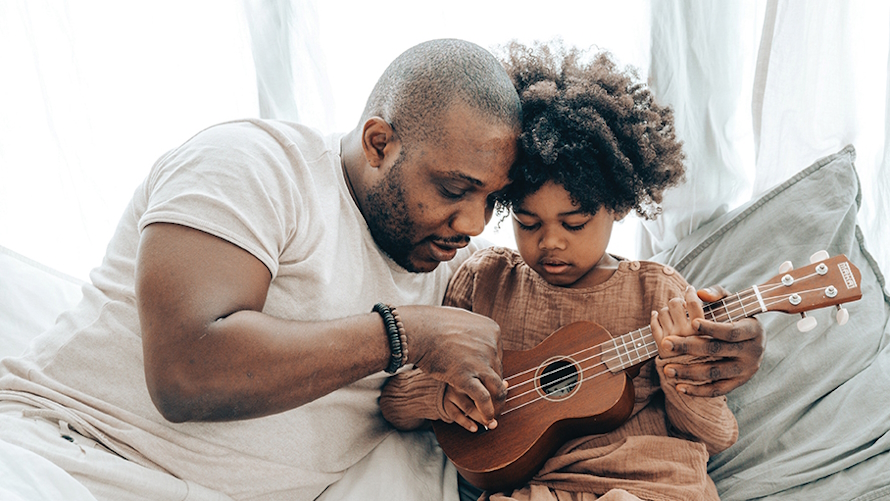 Dad and son sitting together while dad teaches son how to play the ukulele