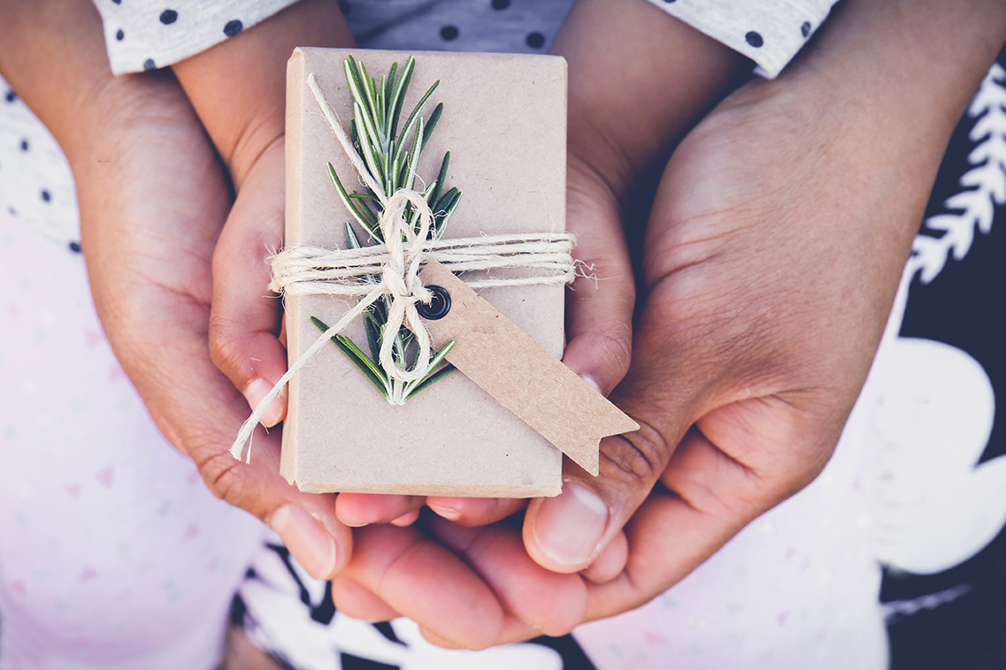 A parent holds her child's hands around a beautifully wrapped holiday present