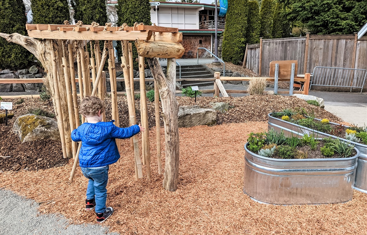 Boy plays with musical sticks sensory play Little Explorers Nature Play Garden PDZA