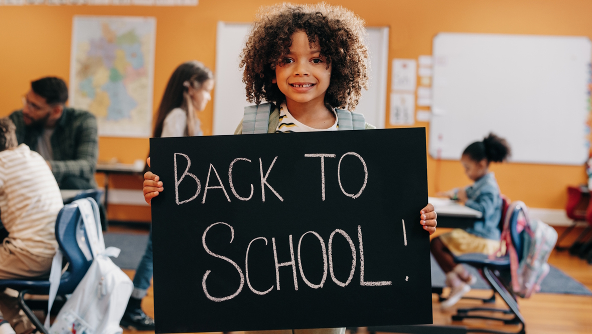 Young girl on first day of school holding up a back-to-school sign