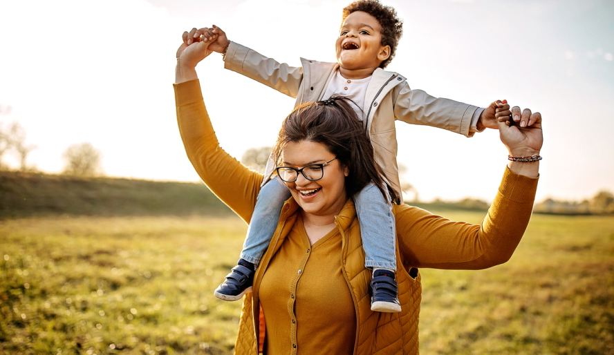 Woman with child on shoulders walking in a field
