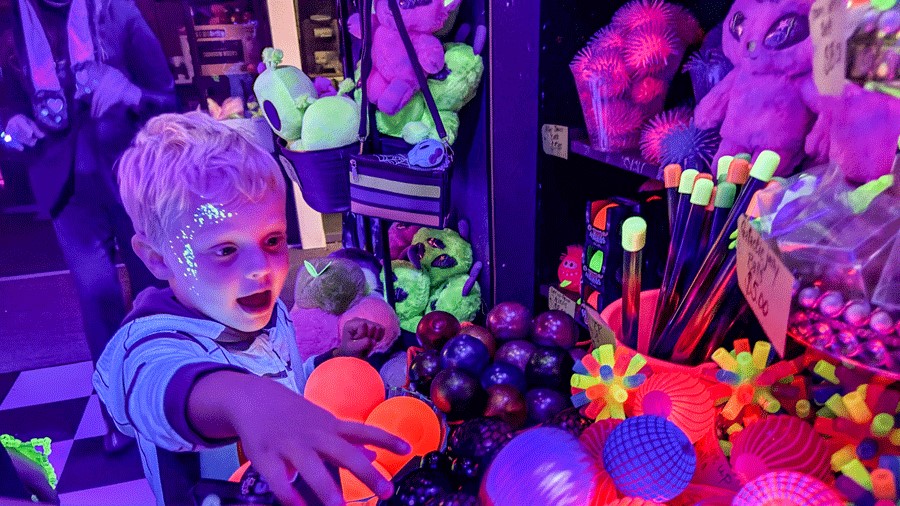 Young boy with face painting looking at glow-in-the-dark toys at Cosmic Carnival