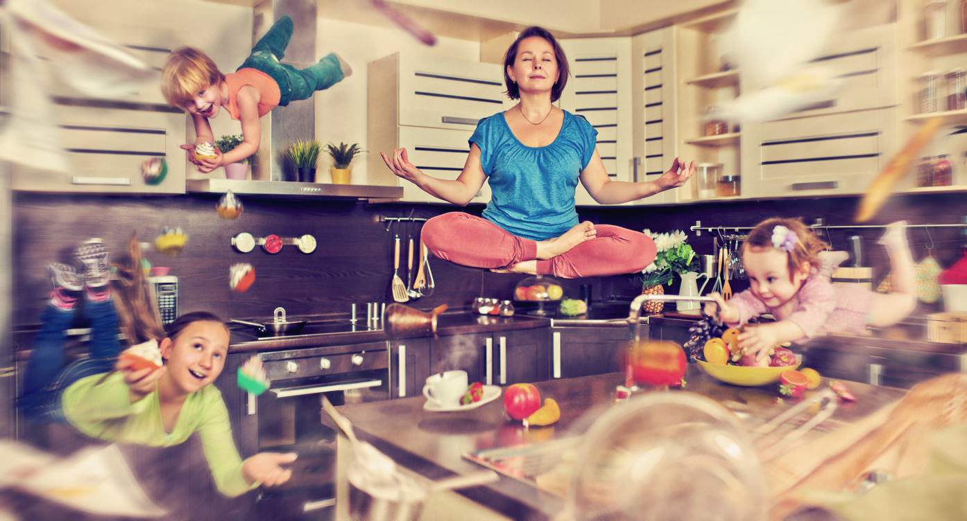 Mother meditating in her kitchen as her three children fly around the room