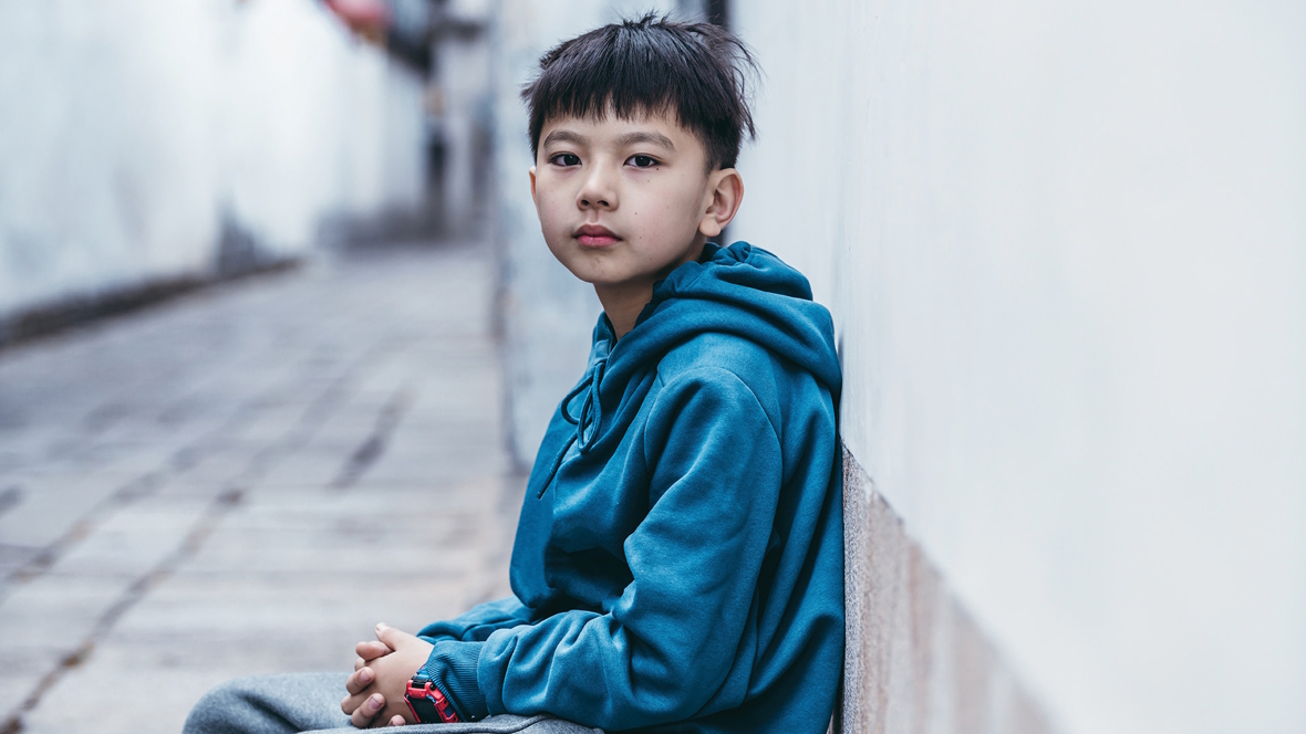 boy sitting next to a wall looking lonely