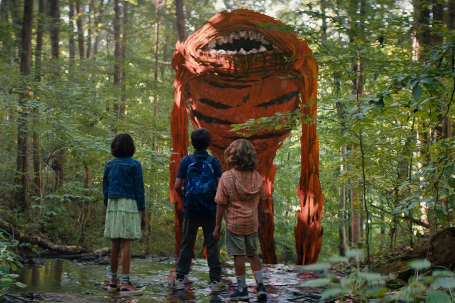 A large orange monster and three kids standing in the wood from the movie “Sketch”