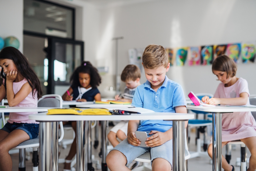 boy looking down at a cell phone in his classroom