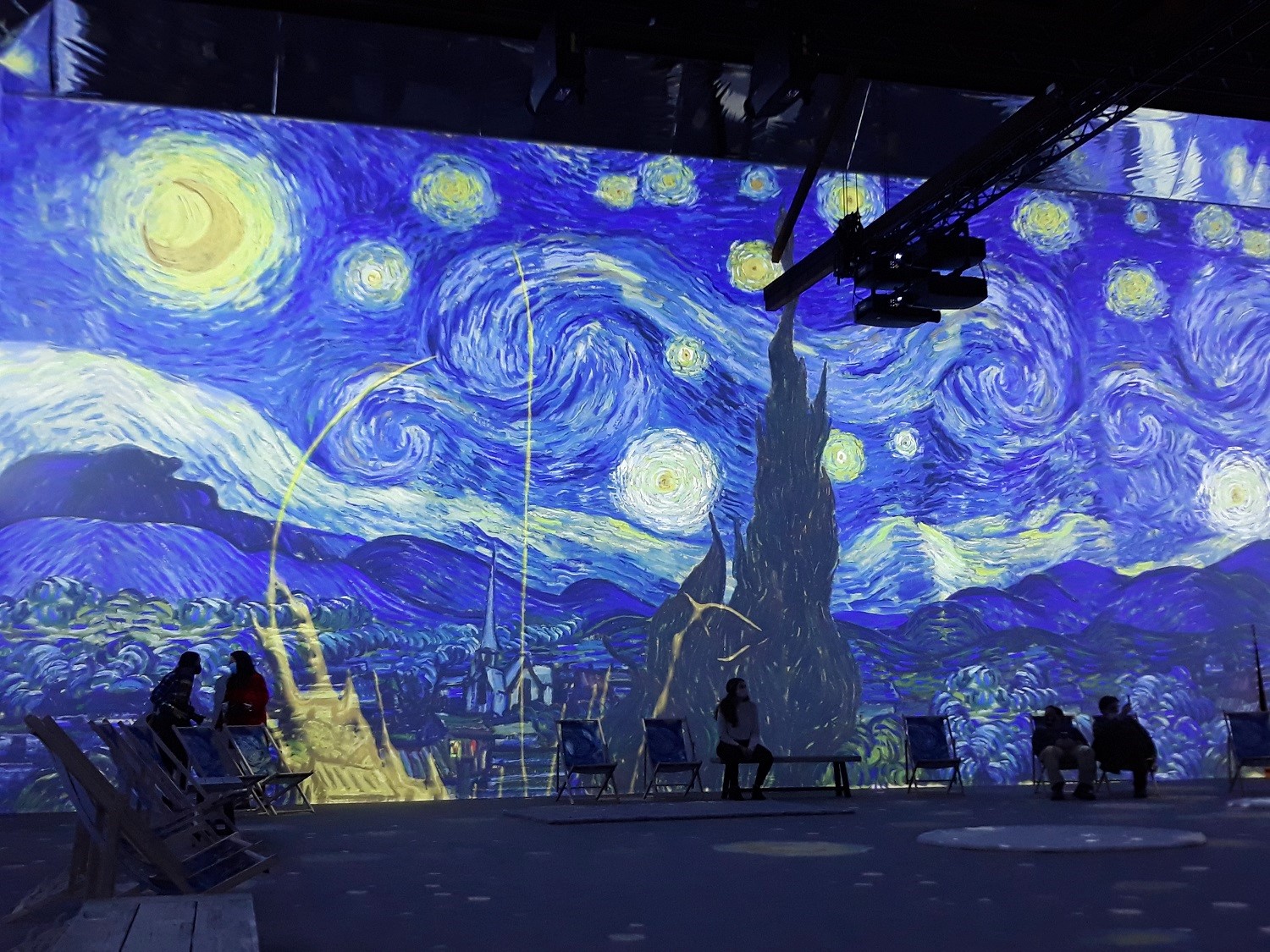 People look on as a digital projection of Van Gogh's Starry Night painting appears on the wall at Van Gogh: The Immersive Experience in Seattle