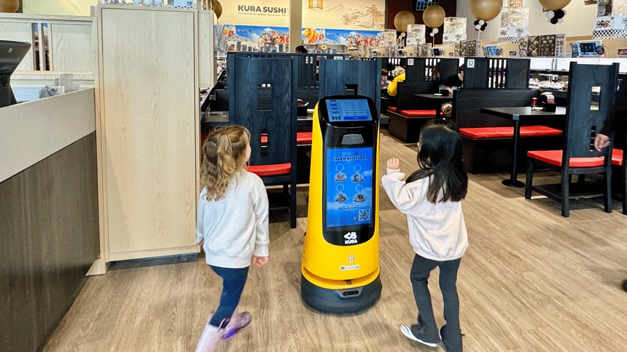 A robot greets two kids at Kura Sushi, a Seattle-area robot restaurant with a sushi conveyor belt
