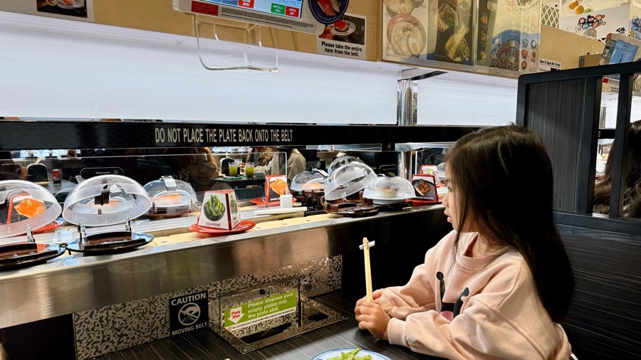 Young girl watches sushi on a sushi conveyor belt at Kura Sushi in Tacoma