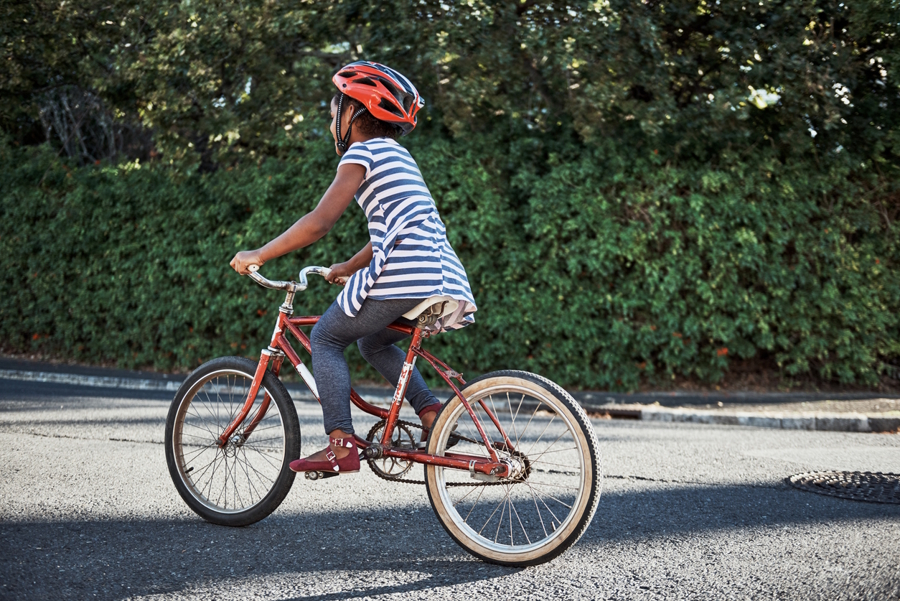 Childing riding a red bike alone on the sidewalk