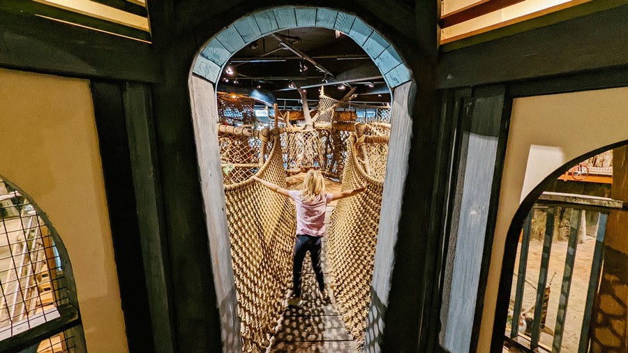 A young girl at Imagine Children’s Museum in Everett climbs a rope tunnel across the treehouse exhibit