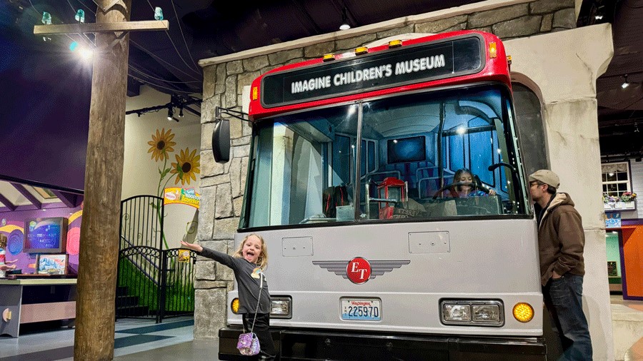 Young girl at Imagine Children’s Museum in Everett poses in front of the museum’s transit bus exhibit