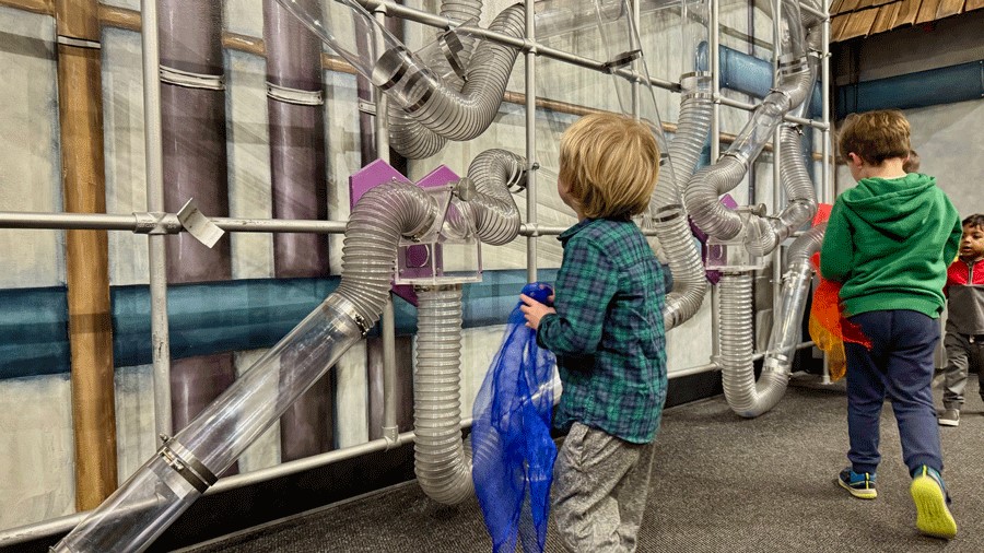 Young boy watches scarves pass through air tube tunnels at Imagine Children’s Museum in Everett