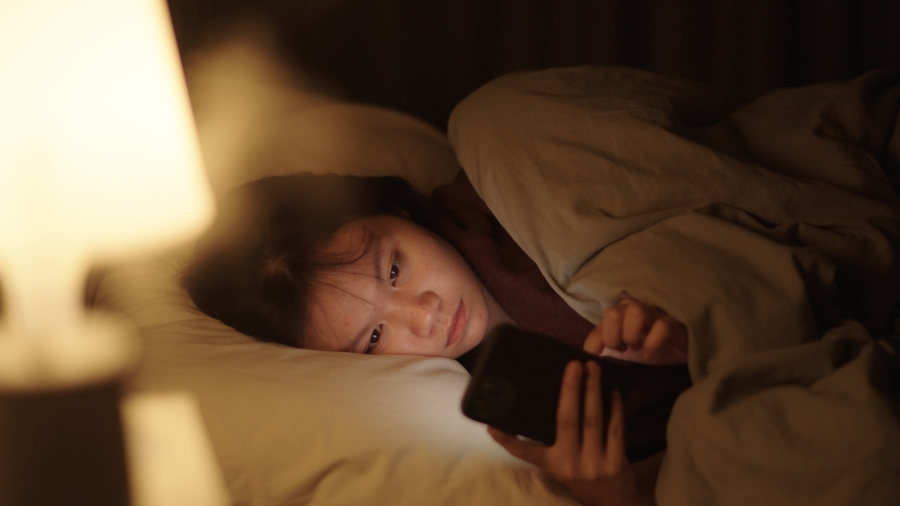 A girl lying in bed at night looking at her cell phone and Instagram Teen Acount