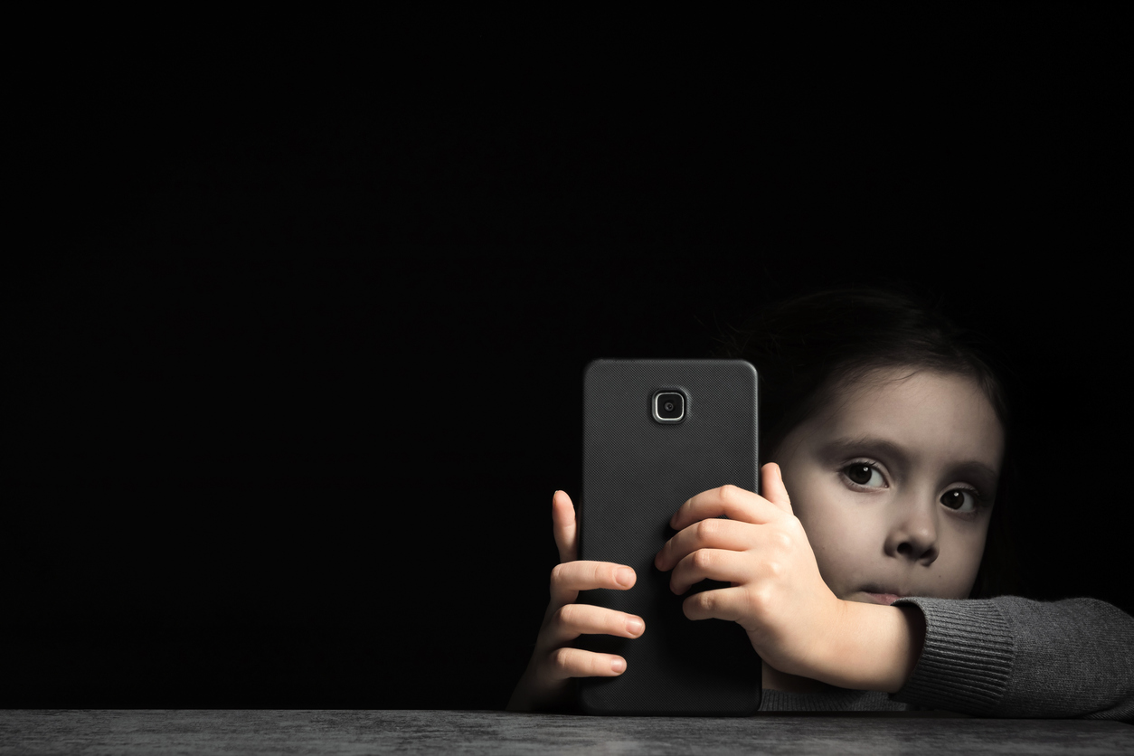 a young child from the anxious generation with a cell phone in hand against a dark background