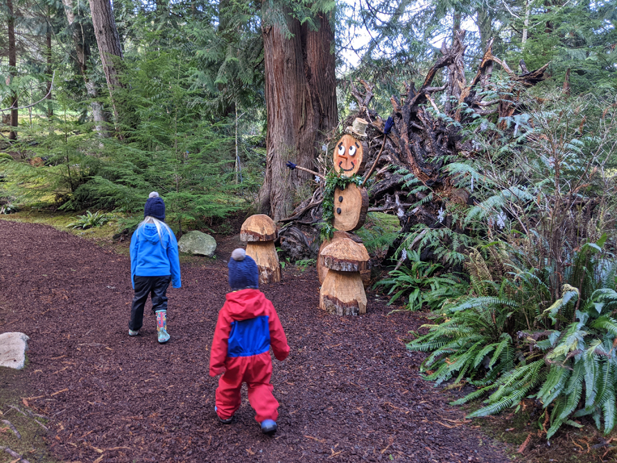 kids walking past snowpeople made of wood