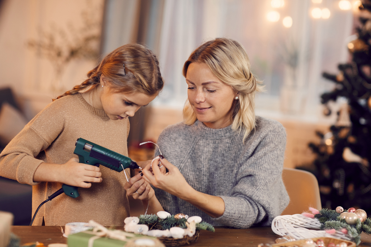 mother and daughter doing a craft with a hot glue gun with a christmas tree in the background