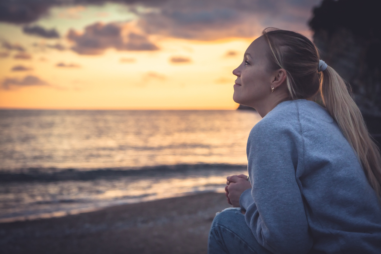 hopeful content woman on a beach smiling at a sunset horizon