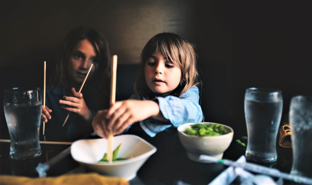 Two kids are eating in a restaurant with their family trying new foods using chopsticks best global dining destinations Seattle families