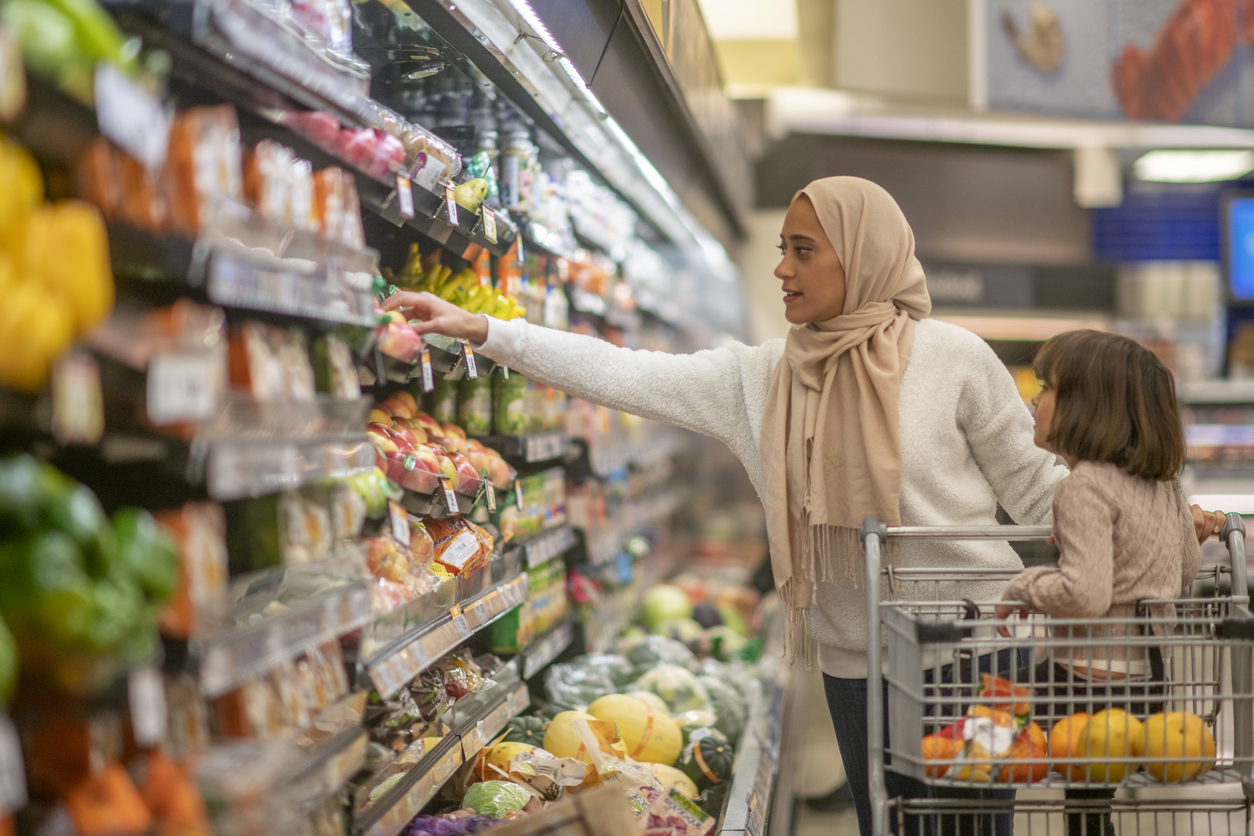 Woman shopping in a grocery store with daughter riding in the cart