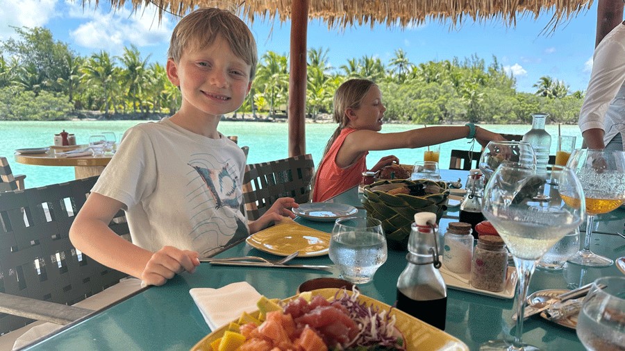 Boy smiling, eating lunch by the water in French Polynesia