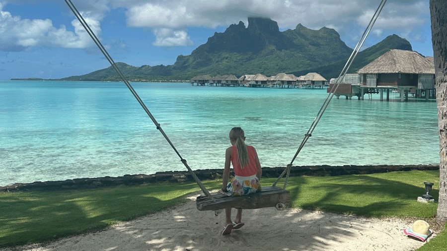 Girl sitting on swing looking at beach and bungalows in Bora Bora