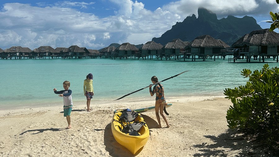Three kids playing on the beach with a yellow canoe