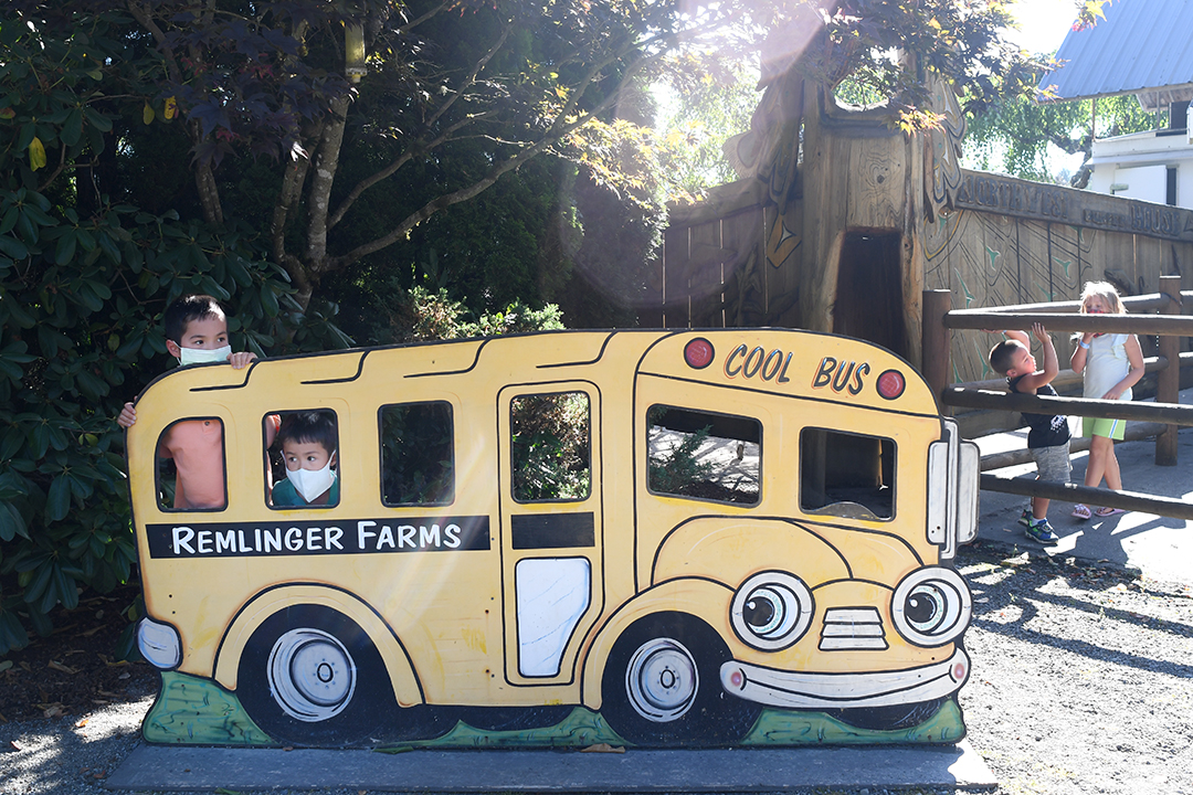 Two adorable brothers peep through the windows of a school bus cutout at Remlinger Farms Fun Park