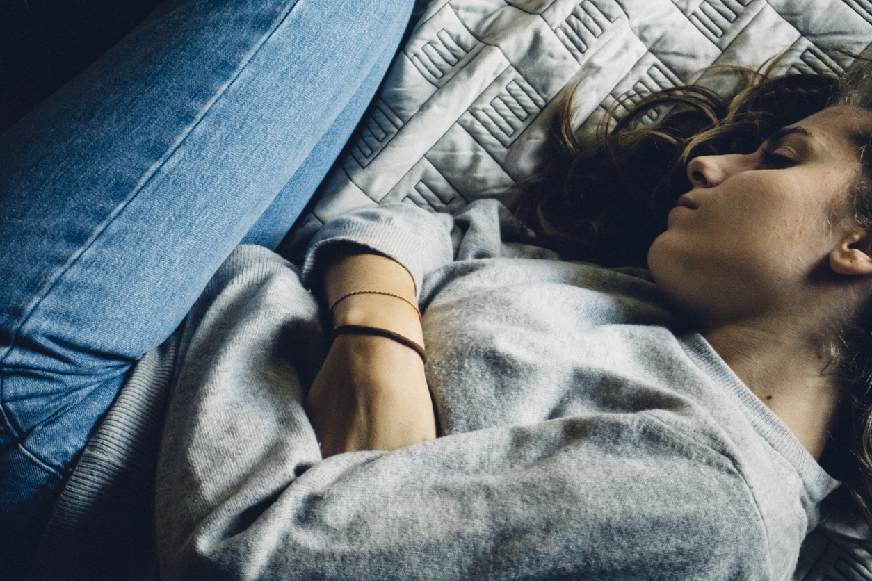 depressed teenaged girl lying on her side on a bed