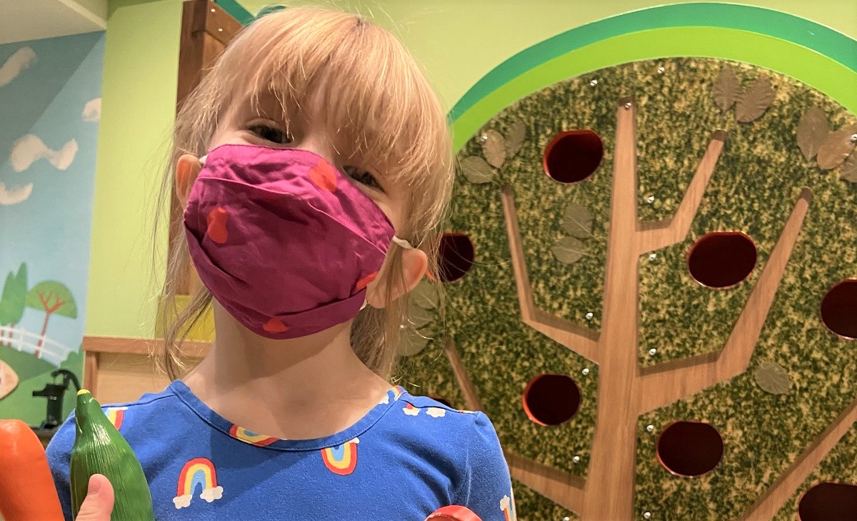 Happy young girl wearing a face covering at KidsQuest Children's Museum in Belleuve reopening after pandemic closure