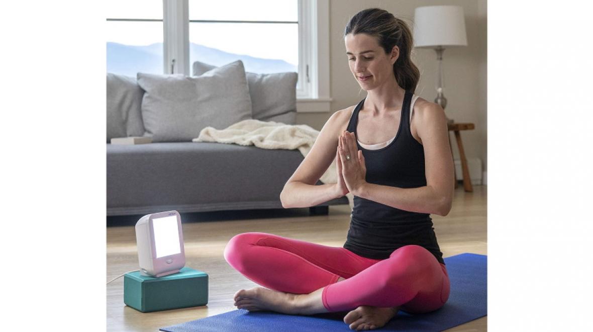 woman sitting cross-legged on a yoga mat in front of a happylight