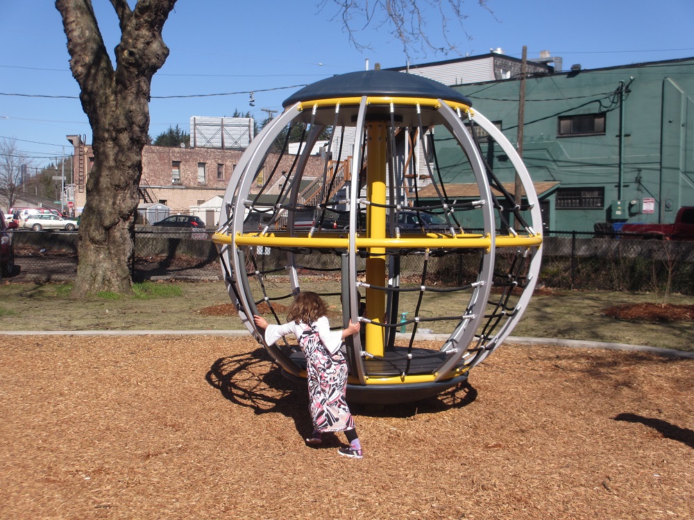 Girl on spinning merry-go-round climber at Georgetown Playfield Seattle playgrounds reopening October 6, 2020