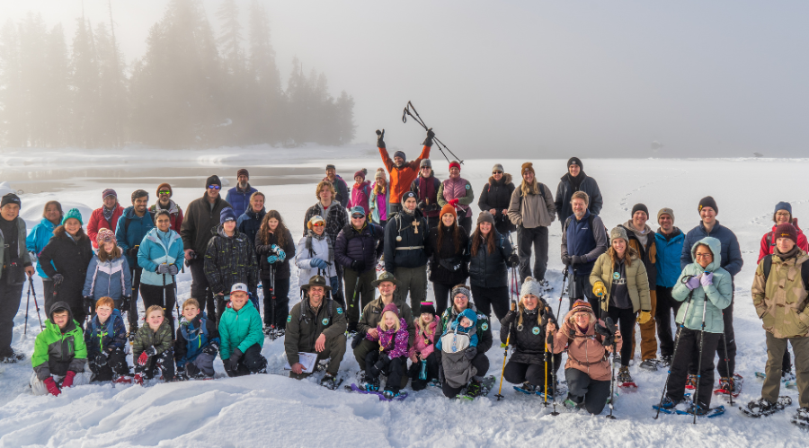 A group of people dressed in winter gear and snowshoes stand in the snow.