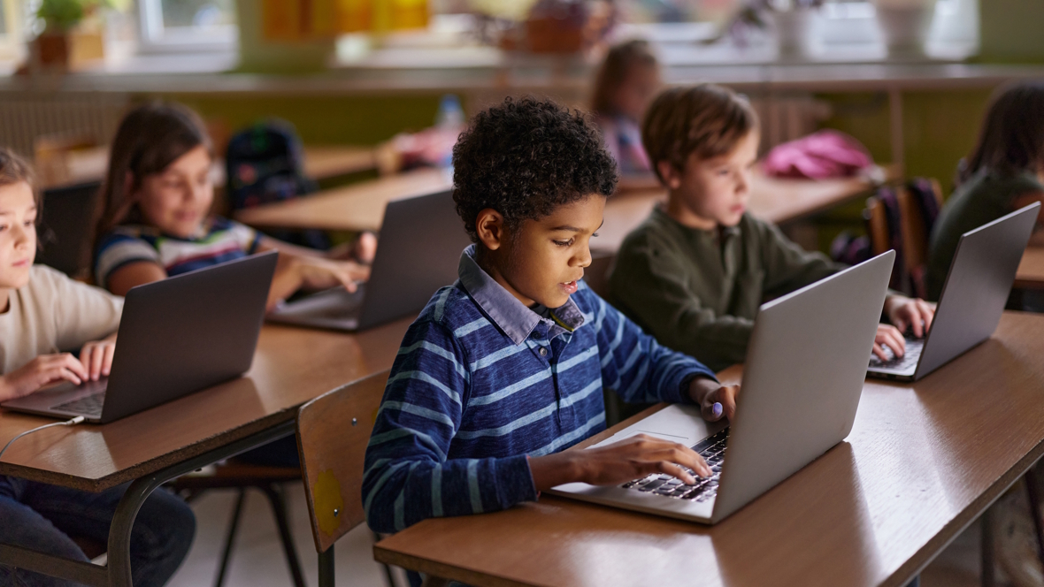 Kids sitting in a classroom all looking at laptops