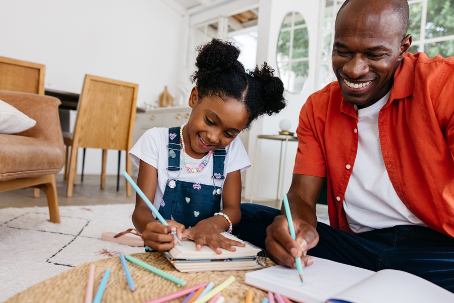 Happy dad and daughter sitting on the floor drawing in notebooks
