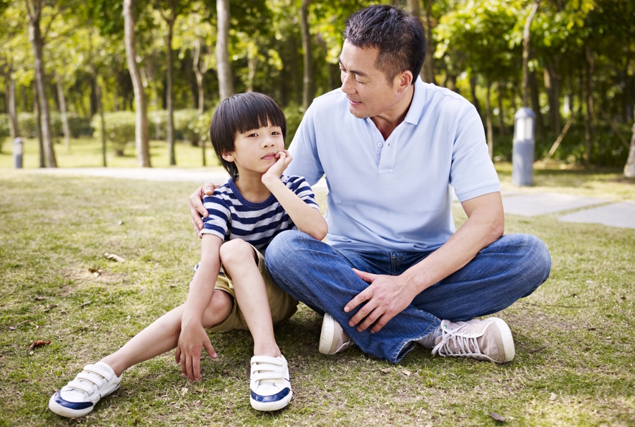 Dad and son sitting on the grass at a park talking
