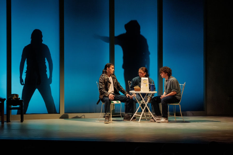 Cast members sitting at a table on stage in The Outsiders