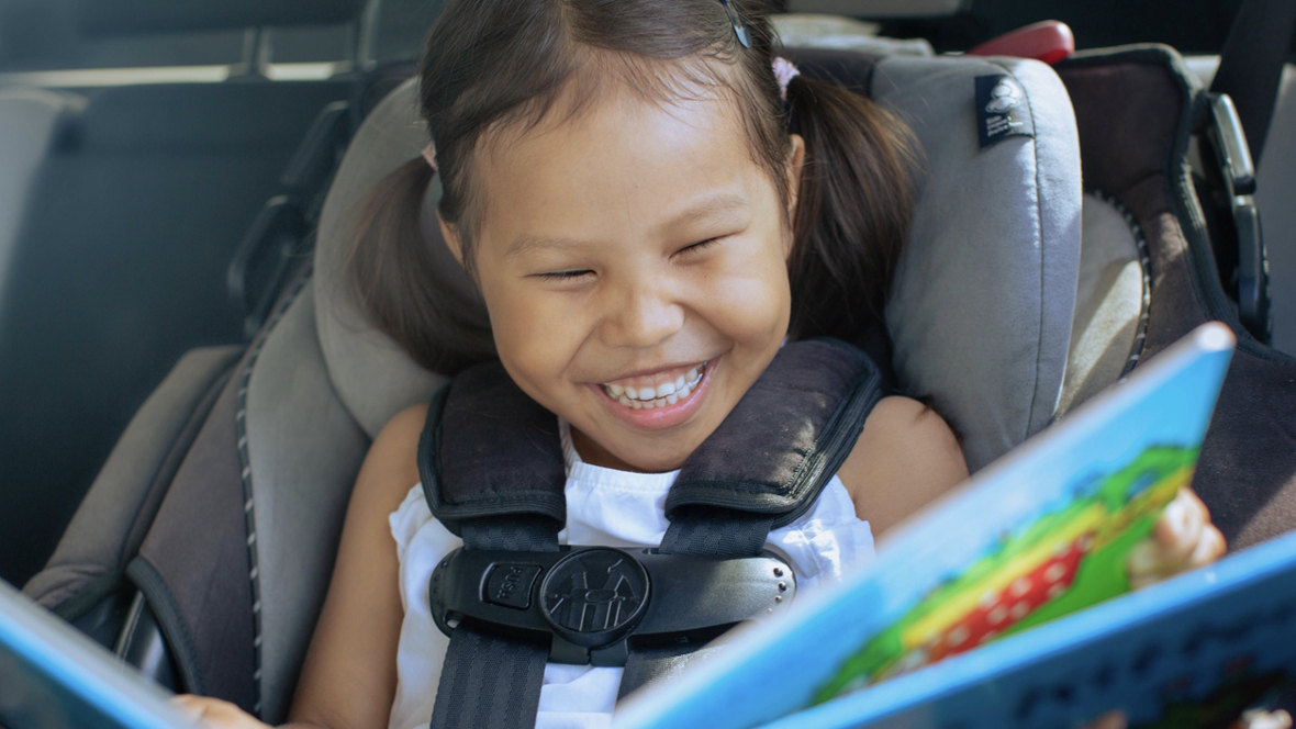 girl in a car seat with a fun car toy happy on a road trip