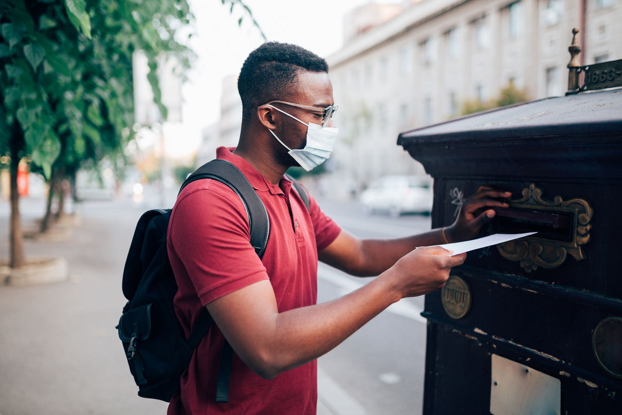 black teen wearing a mask putting his ballot in the mail