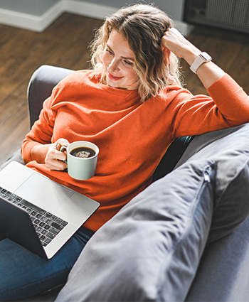 Woman on couch on laptop with a coffee cup