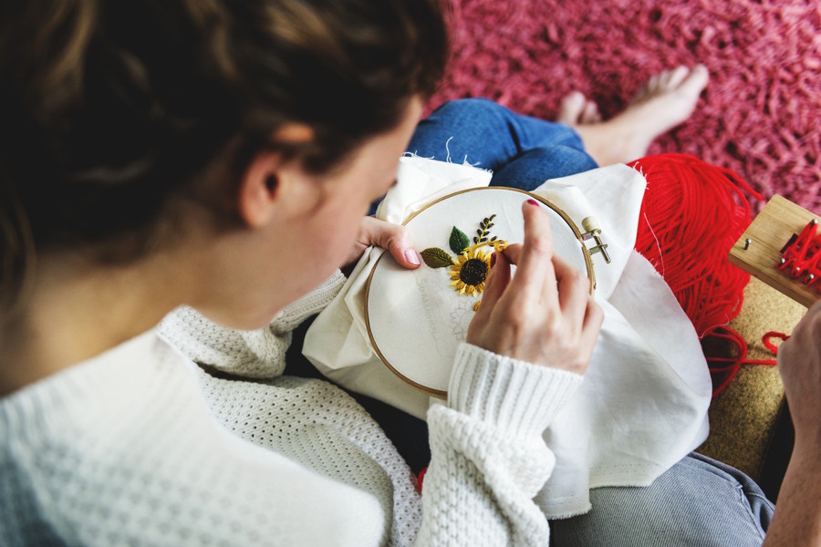 a girl is trying an analog hobby and cross stitching a sunflower