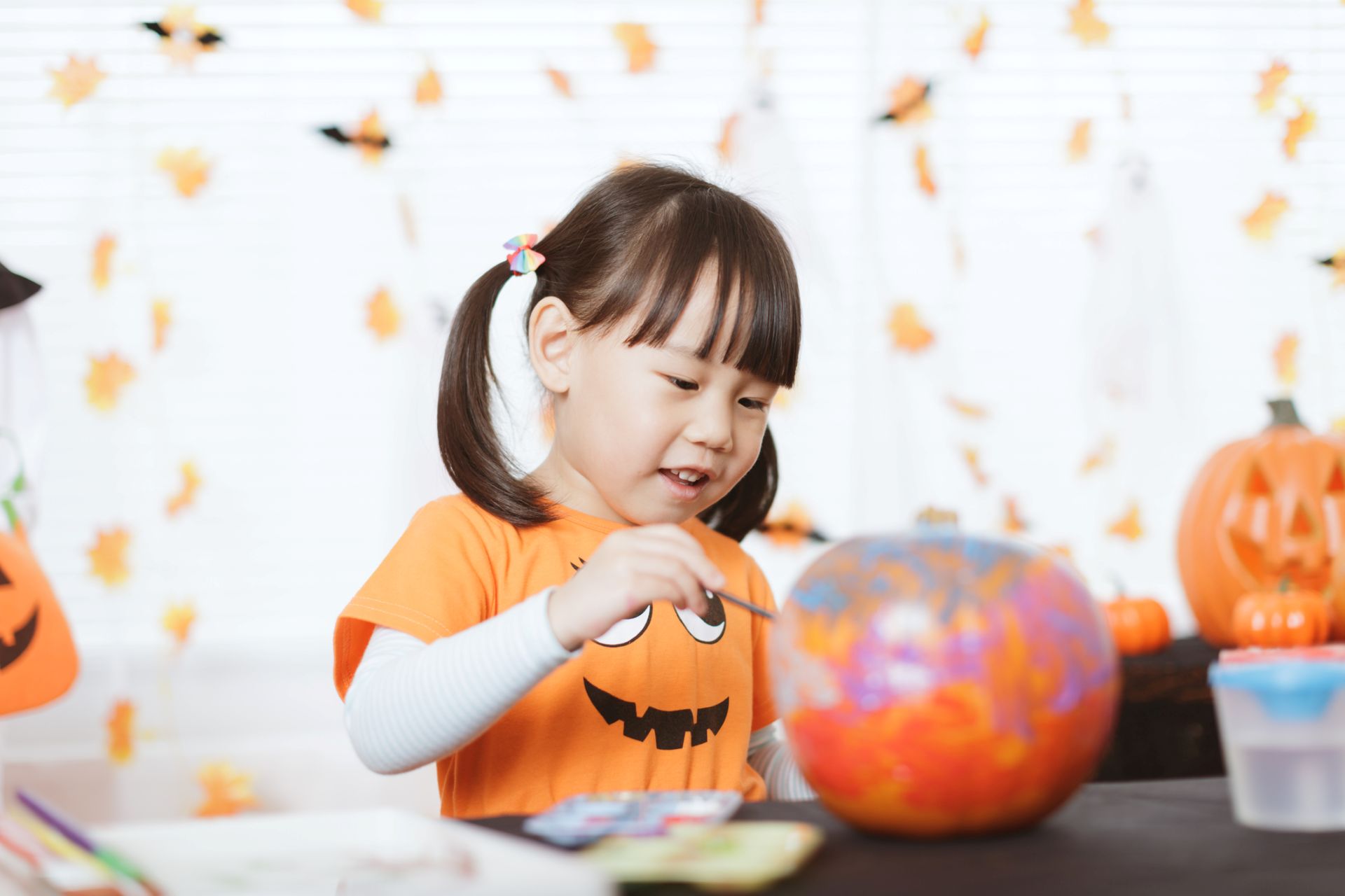 Young girl decorates a pumpkin using paint.