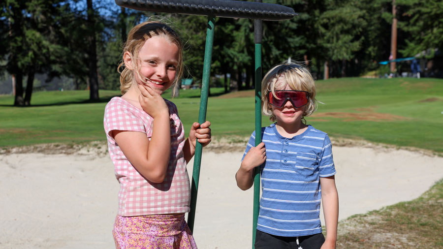 kids standing in front of sand on golf course holding rakes