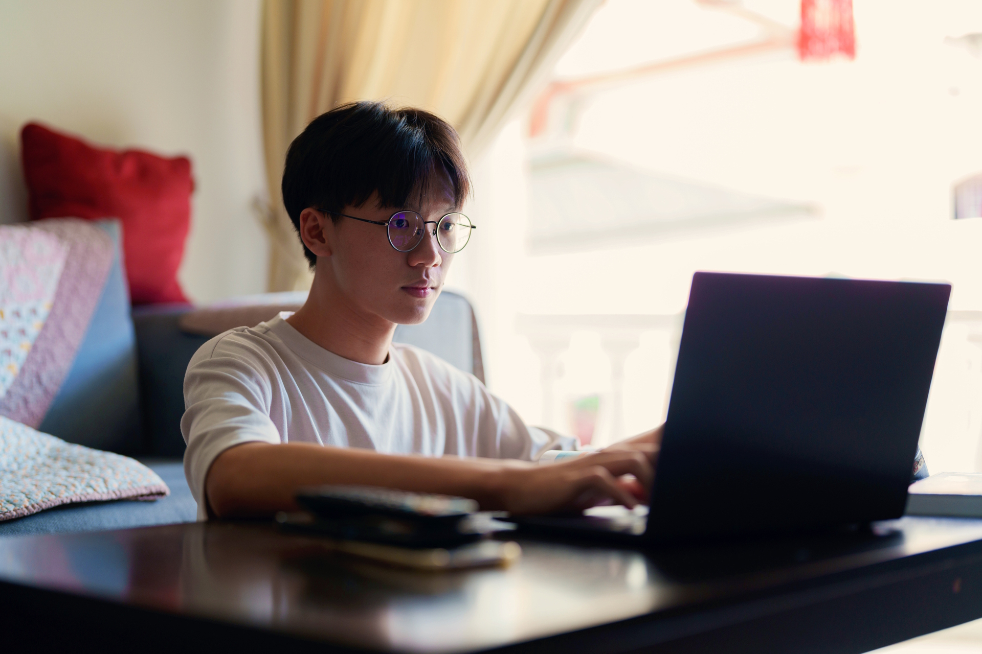 boy typing on a laptop computer near a window at home