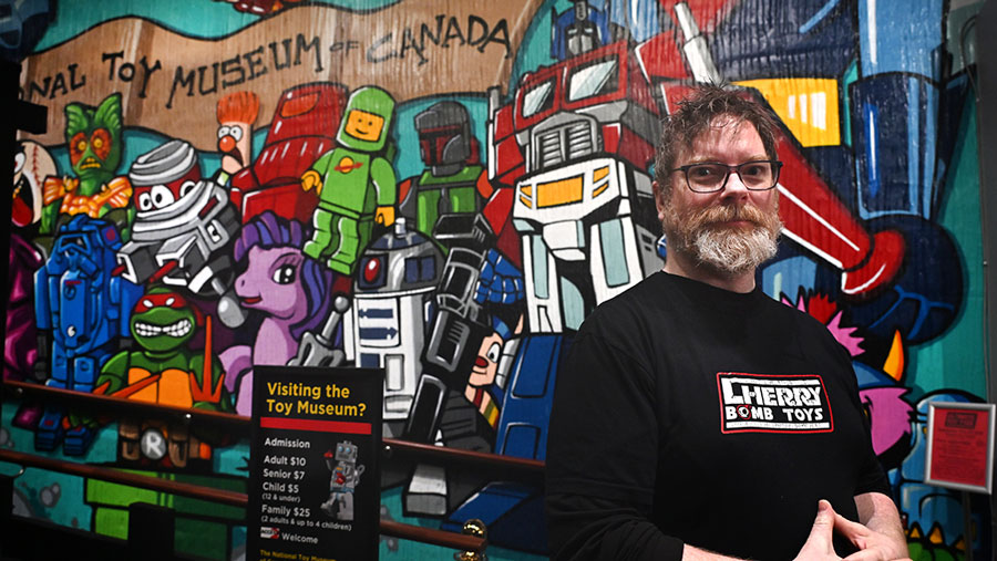 Cherry Bomb Toys ownder B Woodward standing in front of a toy museum mural