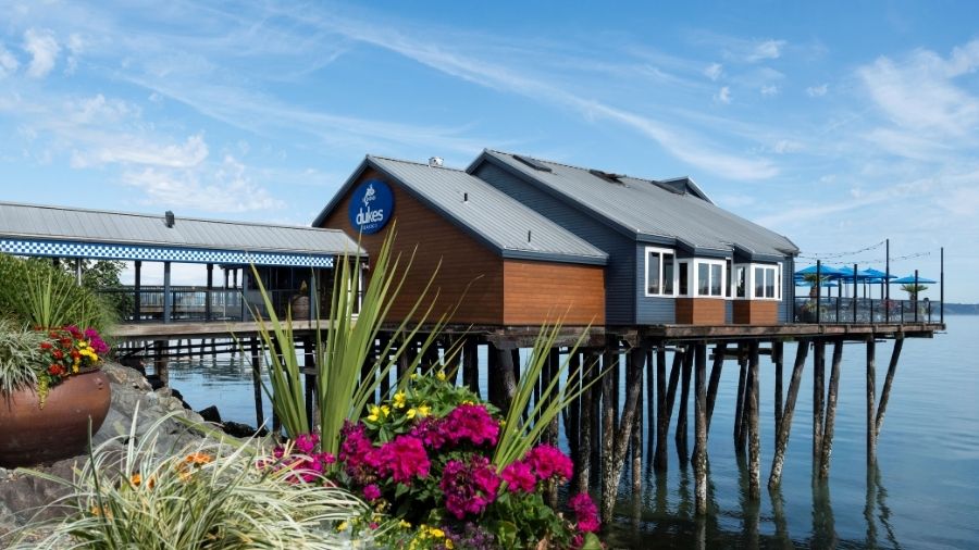 duke's seafood restaurant extending over the water on wooden pilings in tacoma, with colorful flowers in the foreground